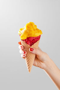Cropped hand of woman holding ice cream cone against white background