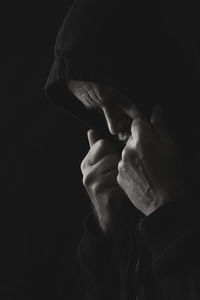 Close-up of man wearing hood against black background