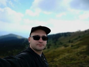 Portrait of mid adult man wearing sunglasses standing on mountain against sky