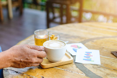 Cropped hands of man holding coffee cup on table at cafe
