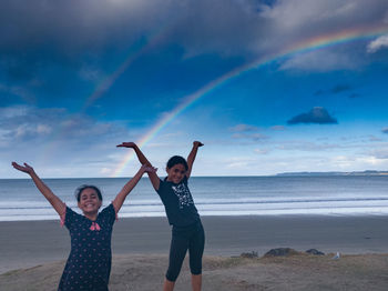 Full length of happy friends on beach against sky