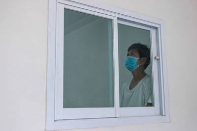 Man wearing flu mask looking through window at home