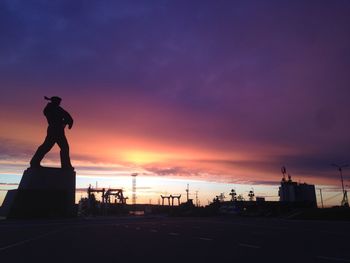 Silhouette man standing on street against sky during sunset