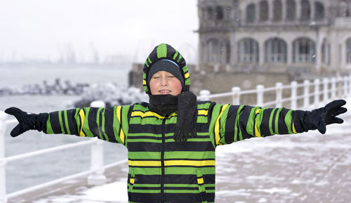 Happy boy with arms outstretched standing on walkway during snowfall