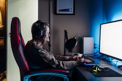 Senior woman wearing headphones using computer while sitting at table