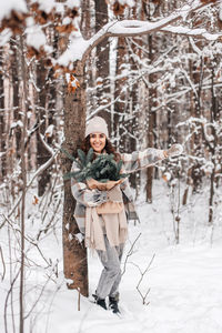 A cute girl in a hat walks in a snowy forest with branches of fir nordic trees nobilis and smiles