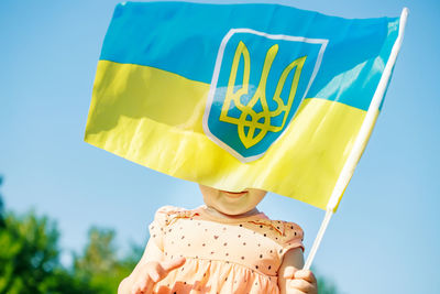 Rear view of woman holding flag against sky