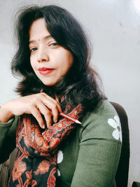 Portrait of beautiful woman holding pencil against wall