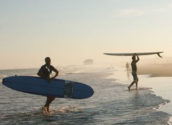 Men working on beach against sky during sunset