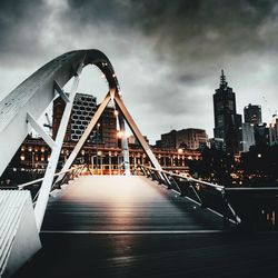 View of footbridge in city against cloudy sky