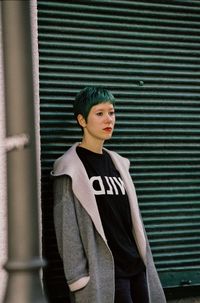 Punk woman standing against green shutter