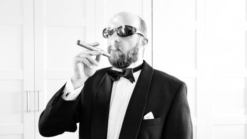 Man wearing sunglasses smoking cigar against wall