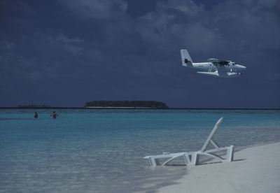 Seaplane flying over sea against cloudy sky