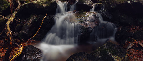 Panoramic long-exposure of a waterfall in the german black forest with rocks and wood