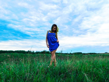 Smiling young woman posing on grassy field against cloudy sky