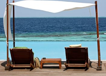 Lounge chairs by infinity pool against clear sky