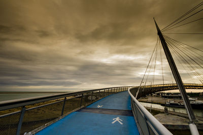 Footbridge at commercial dock against cloudy sky during sunset