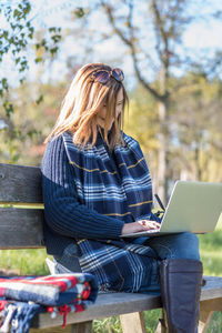 Mature woman using laptop while sitting on bench in park