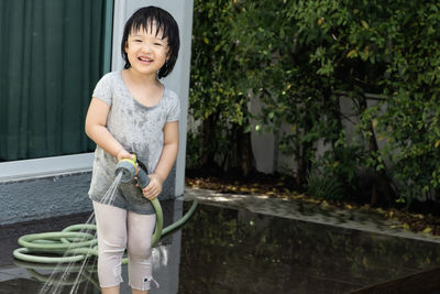 Funny moment of 3 year old asian kid playing water with garden hose in backyard. 