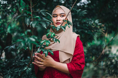 Portrait of young woman standing against trees in forest