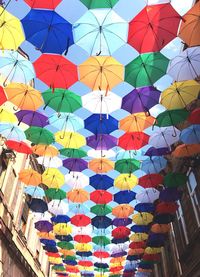 Low angle view of colorful umbrellas hanging amidst buildings against sky