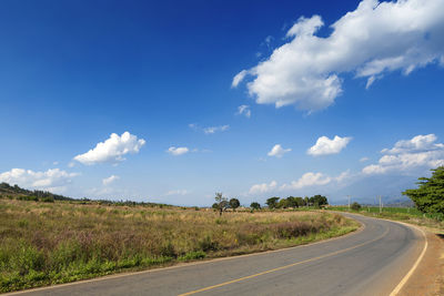 Empty road amidst field against sky