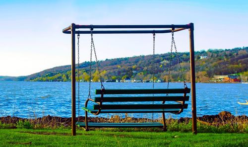 Empty deck chairs by lake against sky