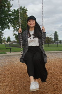 Portrait of smiling young woman on swing in park