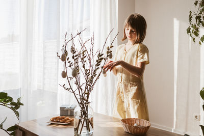 A girl decorates a bouquet of willow with easter eggs at home. decorating your home for the holidays