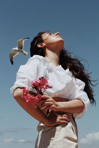 Low angle view of woman holding flowering plant against sky