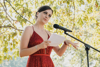 Woman with arms raised standing against tree