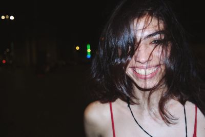 Portrait of smiling woman with tangled hair in city at night