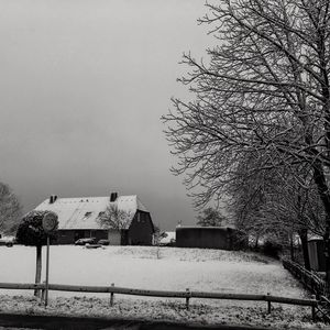 Houses and trees on snow covered field against sky