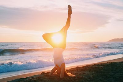 Woman doing yoga on shore at beach during sunset