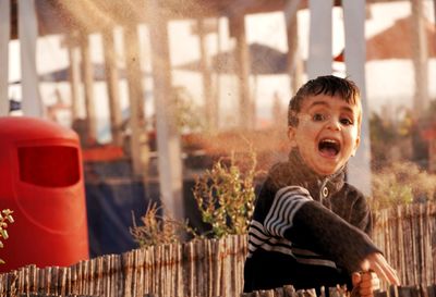 Portrait of happy boy throwing dirt outdoors