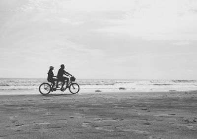 Men riding bicycle on beach against sky