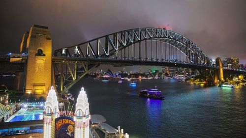 Illuminated sydney harbour bridge over river against sky at night