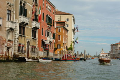 Boats in canal by buildings against sky in city