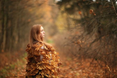 Side view of woman standing against tree during autumn