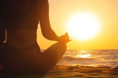 Close-up woman's hand practicing yoga silhouette, meditation in lotus position on the beach, feel so