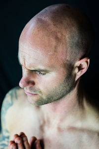 Close-up of shirtless bald man praying against black background