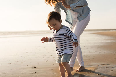 Low section of mother with son walking at beach