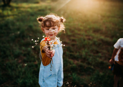 Young girl holding bouquet of wild flowers outside in golden hour