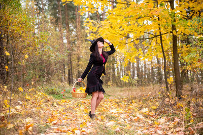 Cheerful smiling young woman surrounded by alling yellow leaves celebrate halloween in witch costume