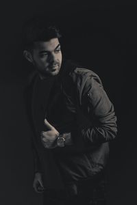 Portrait of young man standing against black background