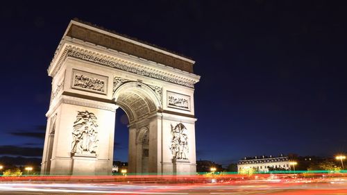 Light trails by arc de triomphe against city during night