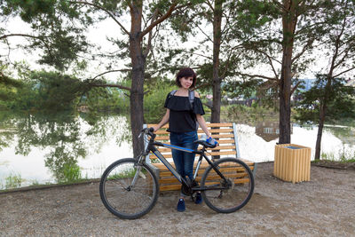 An adult female tourist with a backpack on her back riverbank with a bicycle.