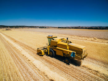 Aerial view of powerful fast yellow vehicle working on field cultivating harvest of wheat