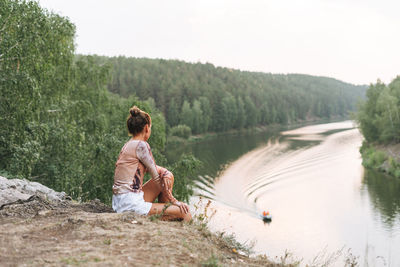 Young slim woman in casual clothes looks at beautiful view of mountains and calm river, local travel