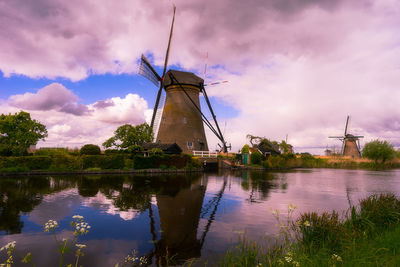 Traditional windmill by lake against sky